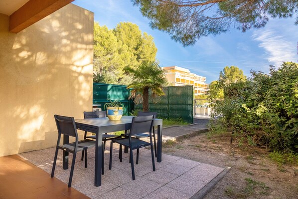 Une terrasse extérieure avec une table et des chaises, un pot de fleurs et une clôture verte.