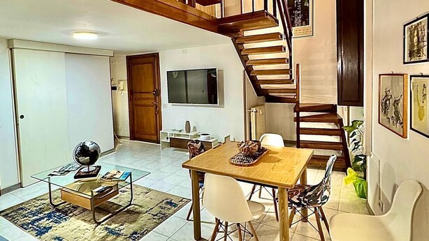 A spacious living area with a wooden staircase, a dining table with chairs, a TV mounted on the wall, and a small globe on a coffee table. - Kevisco House is in the center of Rome very cozy equipped with all the comforts (Roma)
