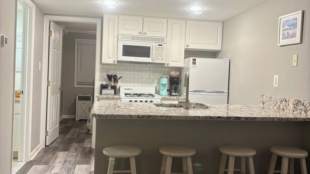 Una cocina con gabinetes blancos, encimera de granito, microondas integrado, estufa a gas y dos taburetes de bar.