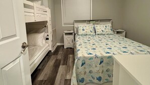 Un dormitorio con una cama doble, una cama individual con colcha estampada, un ventilador de techo y una mesita de noche con lámpara.