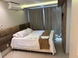 Hotellihuone, jossa on sänky, sängynpääty, yöpöytä, seinään asennettu ilmastointilaite ja verho.