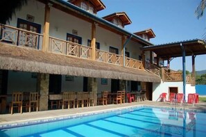 Un hôtel doté d’une piscine, d’un espace extérieur aménagé et d’une structure au toit de chaume.