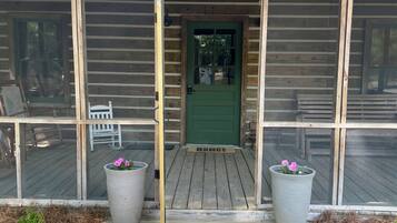 Una cabaña de madera con puerta verde, un porche de madera y dos macetas grandes.