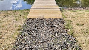 Una banchina in legno che conduce a uno stagno con una fontana, circondato da alberi.
