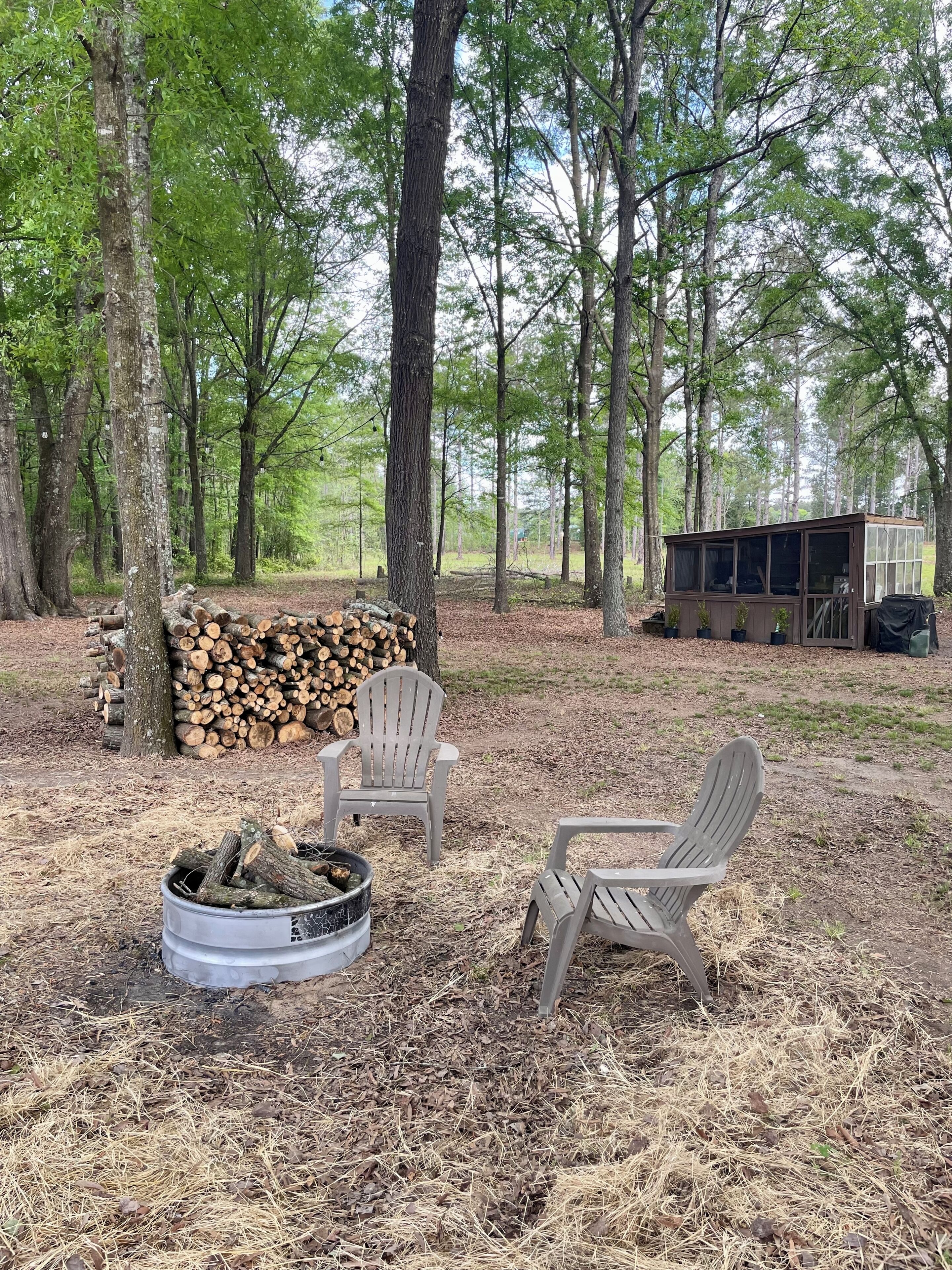 Un camping con dos sillas Adirondack, un hogar para fogata y una cabaña pequeña con puerta de vidrio.