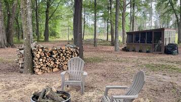 Un camping con dos sillas Adirondack, un hogar para fogata y una cabaña pequeña con puerta de vidrio.
