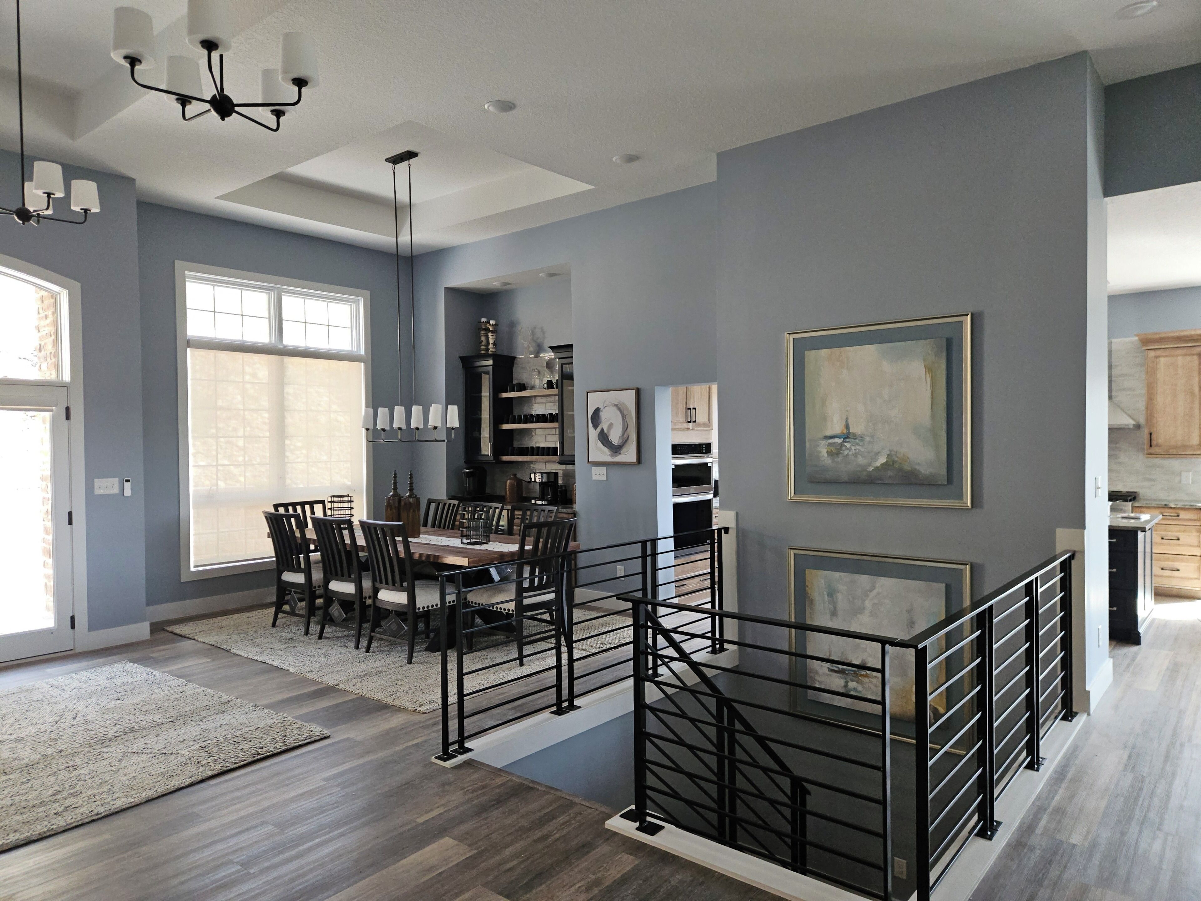 A modern kitchen with built-in appliances, a dining area with a wooden table and chairs, and a staircase with a metal railing.