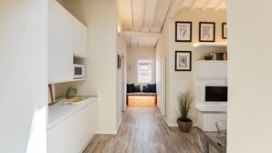 A narrow hallway with a kitchen on the left, a seating area with a window and a plant on the right, and framed pictures on the wall. - Strozzi Terrace View (Firenze)