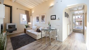 A modern living room with a sofa, a glass dining table with chairs, a fireplace, and a view through an open door. - Strozzi Terrace View (Firenze)