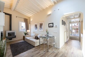 Ein modernes Wohnzimmer mit einer Couch, einem Glastisch mit Stühlen, einem Kamin und Blick durch eine offene Tür.