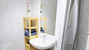 Un baño con lavamanos blanco, muebles de madera y cortina de ducha.