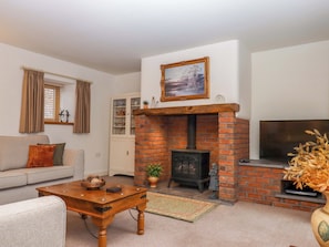 A living room with a brick fireplace, a sofa, a coffee table, and a television. - Grange Cottage (Crediton)
