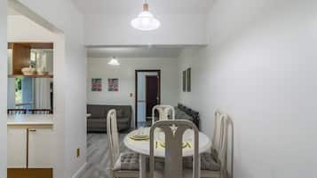A dining area with a round table, chairs, and a light fixture above. There is a sofa and a door leading to another room.
