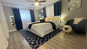 Un dormitorio con cama, mesitas de noche, lámpara, una obra de arte en la pared y ventilador de techo.