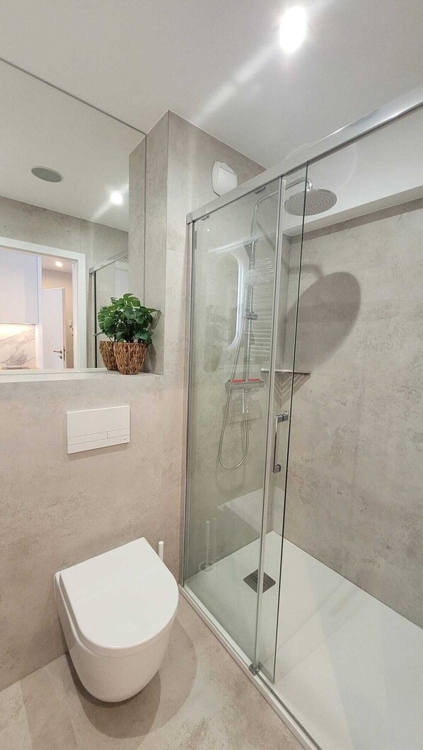 A modern bathroom with a glass-enclosed shower, a white toilet, and a potted plant on the counter.