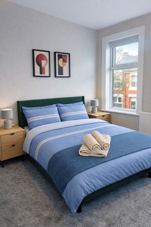 A bedroom with a bed, two bedside tables, a window, and two wall-mounted artworks. - Spacious and New! 3 bed Listing in Manchester. Board games, Smart TV and Guitar! (Manchester)