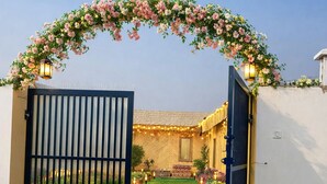 A gated entrance with a tiled pathway leading to a building. - A Rustic Bamboo-Themed Farmhouse in Jaipur with Swimming Pool & Jacuzzi Escape (Rawlot Nagar)