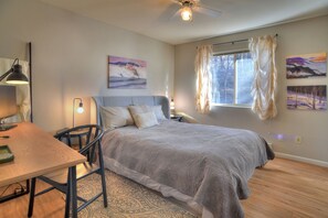Ein Schlafzimmer mit Bett, Schreibtisch, Stuhl, Deckenventilator und Bildern an der Wand.