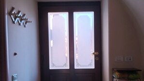 Eine dunkle Holztür mit zwei Glasfeldern, einer kleinen Ablage mit einer Kiste und einem Lichtschalter an der linken Wand.