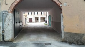 Ein schmaler Gang mit einem Ziegelbogen, der zu einem Gebäude mit weißer Fassade und nummerierten Türen führt.