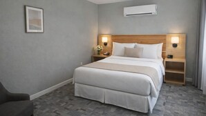 A hotel room with a large bed, two bedside tables, an air conditioning unit, and a framed picture on the wall. - Skyliner Motel (Stroud)