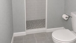 A bathroom with a white toilet, a shower area with a white tiled wall, and a tiled floor. - Skyliner Motel (Stroud)