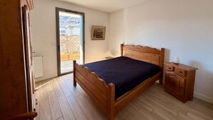 A bedroom with a wooden bed, a nightstand, a radiator, and a door leading to an outdoor area.