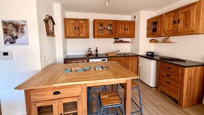 A compact kitchen with wooden cabinets, a central island, stools, and a small refrigerator.