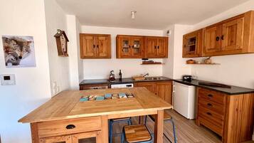 A compact kitchen with wooden cabinets, a central island, stools, and a small refrigerator.