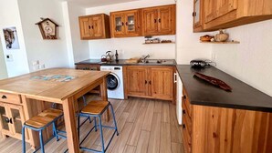 A compact kitchen with wooden cabinets, a washing machine, and a dining area with stools.