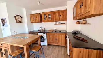 A compact kitchen with wooden cabinets, a washing machine, and a dining area with stools.