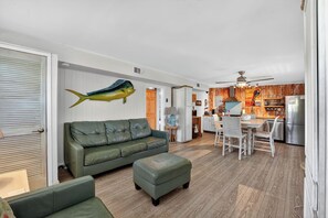 Een moderne woonkamer met een groene bank, een eethoek met witte stoelen, en een keuken met houten kastjes.