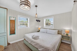 Een slaapkamer met een bed, twee nachtkastjes met lampen, een hanglamp, een raam met jaloezieën en een deur.