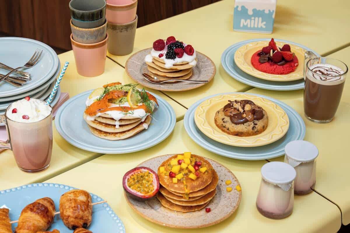 Un bufé de desayuno con diversos platos, como panqueques, gofres y pastelería, además de bebidas y una estación de leche.