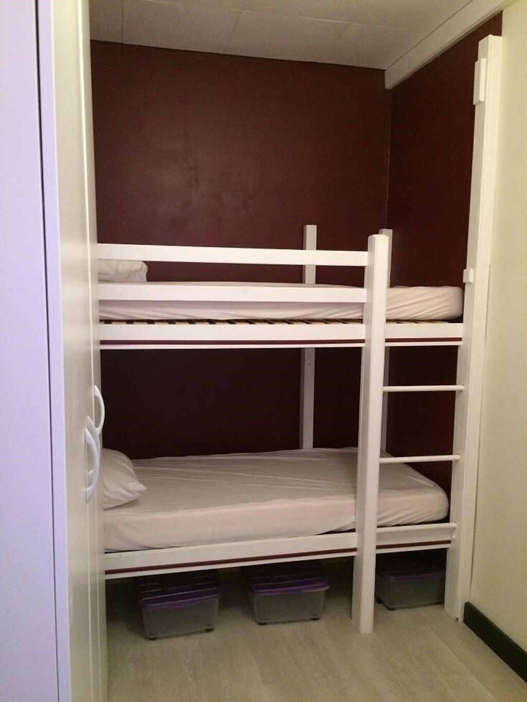 A bunk bed room with a wardrobe and storage bins.