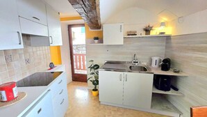A compact kitchen with white cabinets, a sink, and a stove. There is a potted plant and a small table with a kettle and a cup. - Maison Cavalese - Polar Express - Intimacy in the center of town (Cavalese)