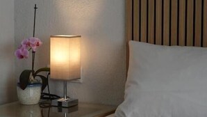 Ein Hotelzimmer mit einem Bett, einem Nachttisch mit Lampe, einer Vase mit Blumen und einem hölzernen Kopfteil.
