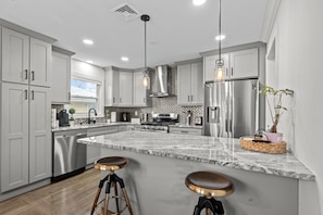Una cocina moderna con electrodomésticos de acero inoxidable, una isla de mármol e iluminación colgante.