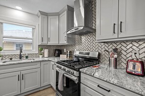 A modern kitchen with grey cabinets, a stainless steel range hood, a gas stove, and a toaster.