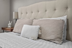 A bed with a tufted headboard, two pillows with tassels, and a bedside table with a lamp.