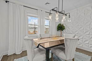 A dining area with a wooden table, white upholstered chairs, and a hanging light fixture.
