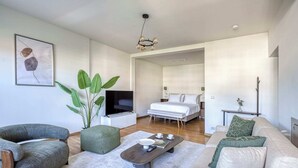 Un salon moderne comprenant un canapé, un fauteuil et un pouf, une table basse, une grande plante et un téléviseur.