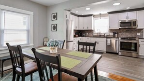 A modern kitchen with white cabinets, stainless steel appliances, and a dining area with a wooden table and chairs.