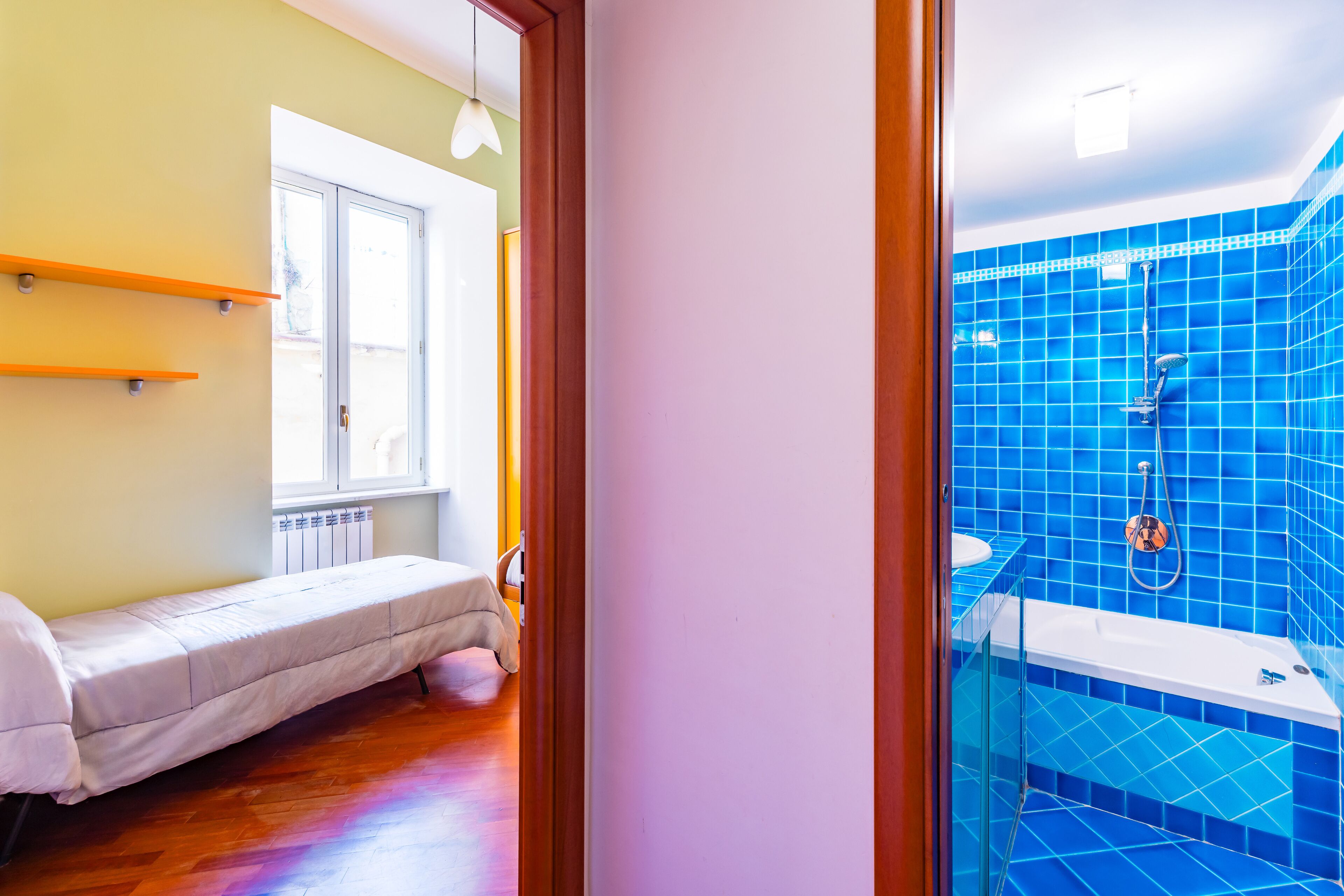 A room with a bed, a window, a shower with blue tiles, and a radiator.