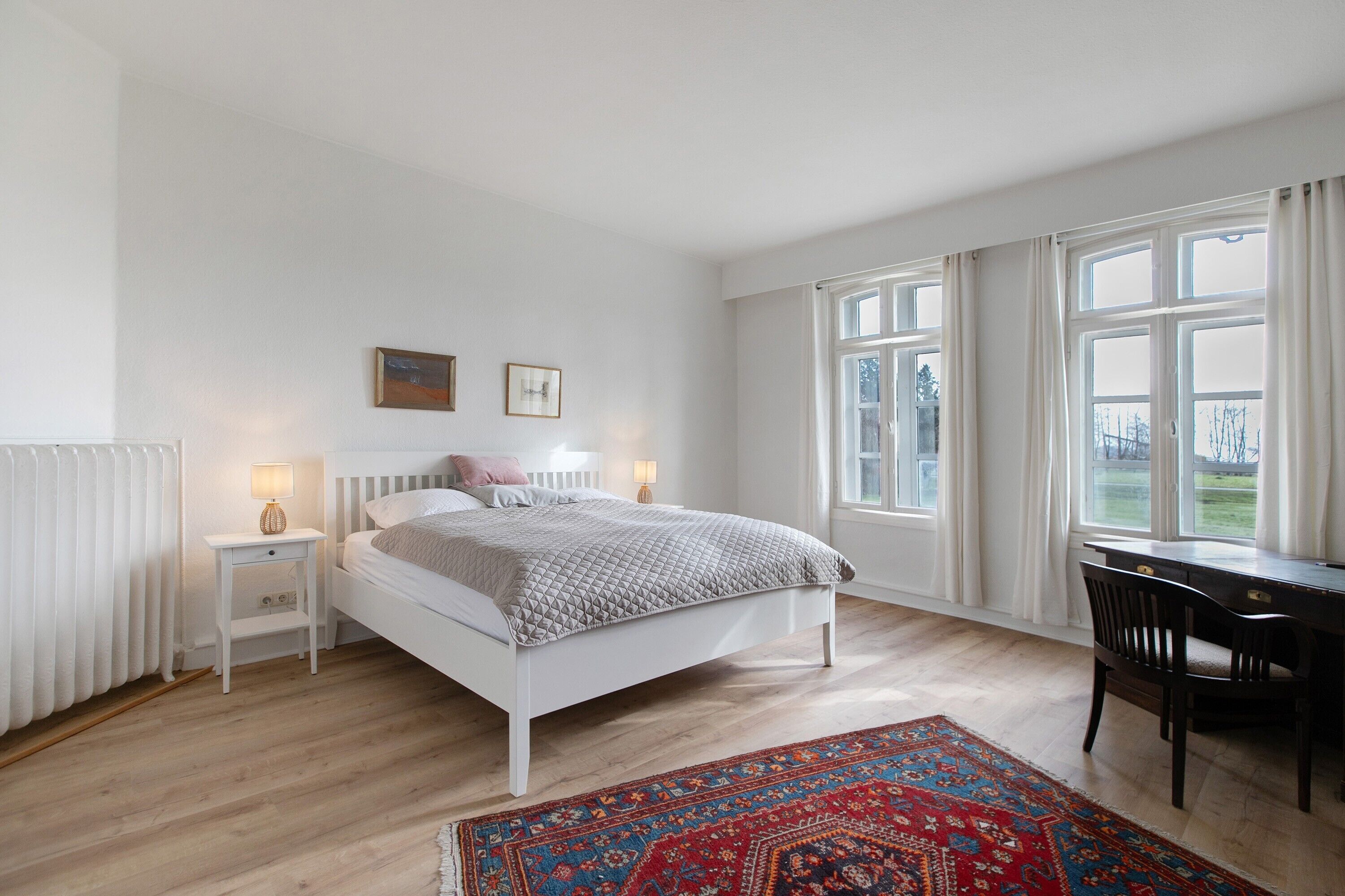 A bedroom with a bed, bedside tables, a desk, and a window.