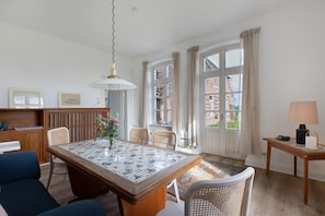 A dining area with a table, chairs, a hanging light fixture, and a view of the outside through large windows.