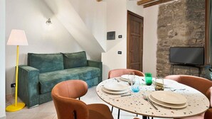 A cozy living area with a green sofa, orange chairs, a round table set with plates and glasses, a floor lamp, and a stone wall with a television. - Nuance, beautiful things are created with colour, harmony and the positive feelings, all that is Nuance the ideal place for your holidays in Corniglia.Located in the centre of the most typical and unique village of Cinque Terre, Nuance will know pamper y (Vernazza)