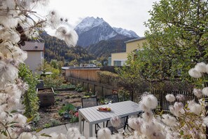 A garden with a table set for dining, surrounded by plants and trees, with a mountain in the background. - Chasa Marugg: Cosy 3.5-room flat right next to Engadin Bad Scuol (Scuol)