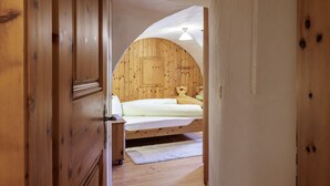 Ein Schlafzimmer mit Holzbalkendecke, einem Bett mit weißer Matratze und grüner Decke sowie einem Holzschrank.