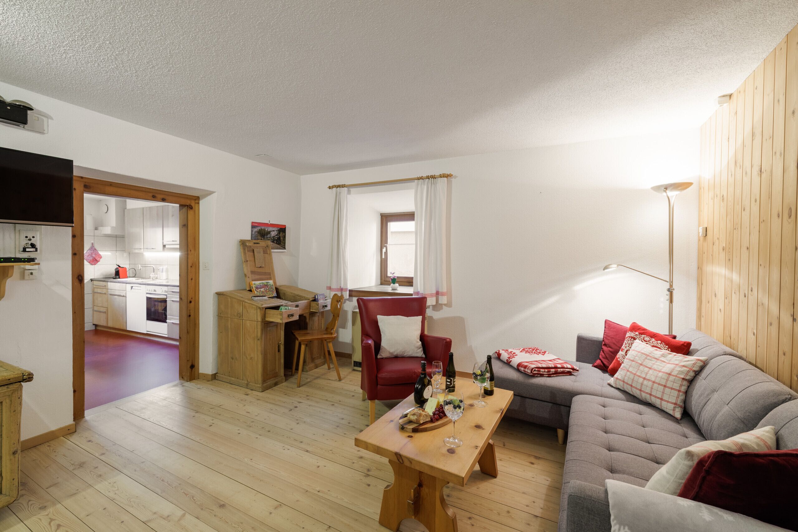 A cozy living room with a sofa, a dining table with a red chair, and a kitchen visible through an open door.